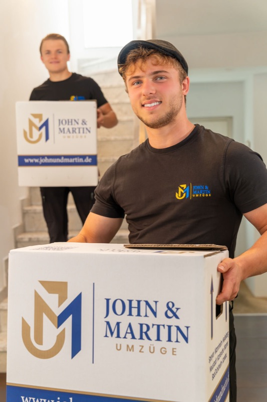 Zwei Mitarbeiter mit Umzugskartons von John & Martin im Treppenhaus.