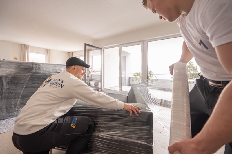 Zwei Mitarbeiter verpacken ein Sofa in Stretchfolie.